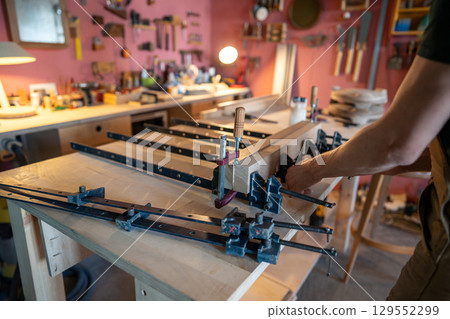 Builder hands press wooden pieces with clamps after apply adhesive for sturdy board. Surface smooth 129552299
