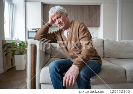 Depressed apathetic old man resting head in hand sitting alone on couch with blank stare at home Depressed apathetic old man resting head in hand sitting alone on couch with blank stare at home 129552300