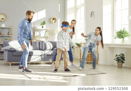 Large joyful family plays blindfolded games in living room. Children and parents participate in timeless games of blind man's buff game bringing light energy to family gathering Blind Man's buff game. 129552308