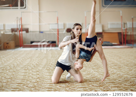 Coach with student. Girls gymnasts, performs various gymnastic exercises and jumping. Childs and sport, a healthy lifestyle. Coach with student. Girls gymnasts, performs various gymnastic exercises and jumping. Childs and sport, a healthy lifestyle. 129552676