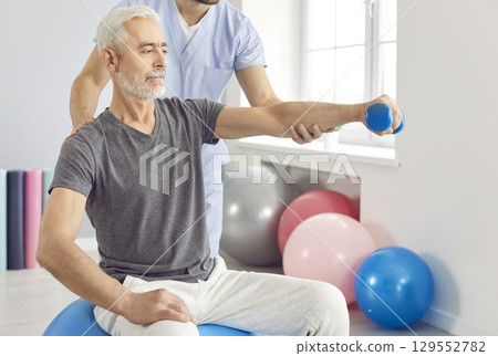 Physician or physiotherapist helping patient to do exercises with dumbbel during arm rehabilitation. 129552782
