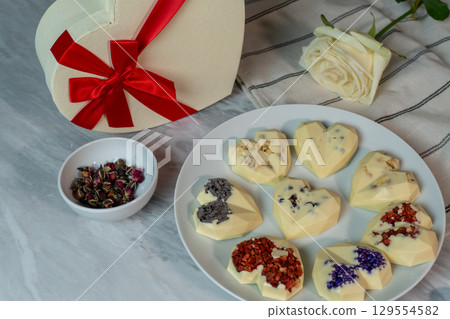 Heart-shaped chocolates with floral decoration on marble table with rose and gift box Heart-shaped chocolates with floral decoration on marble table with rose and gift box 129554582