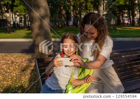 Mother and daughter enjoying outdoor moments on a park bench Mother and daughter enjoying outdoor moments on a park bench 129554594