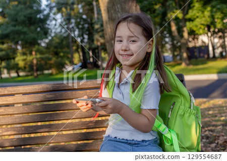 Smiling child with backpack using smartphone in park on sunny day 129554687
