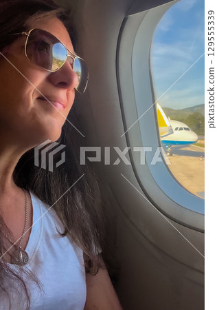 Woman looking out the airplane window, before takeoff. Vertical shot. Copy space Woman looking out the airplane window, before takeoff. Vertical shot. Copy space 129555339
