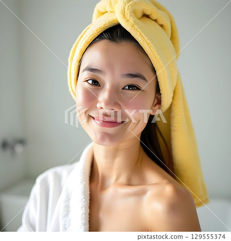 Portrait of young woman with towel on head in white terry robe, spa treatments and skin care on light background Portrait of young woman with towel on head in white terry robe, spa treatments and skin care on light background 129555374