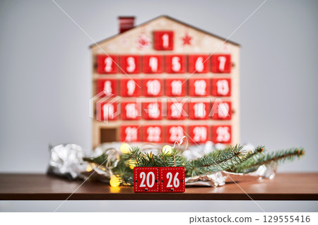 Christmas Advent calendar in the shape of a house with boxes making up the number 2026. 129555416