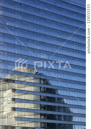 The facade of a modern multi-storey building with reflections in the windows 129555533