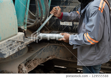 A mechanic is adding grease to a hydraulic cylinder of a machine. A mechanic is adding grease to a hydraulic cylinder of a machine. 129555588
