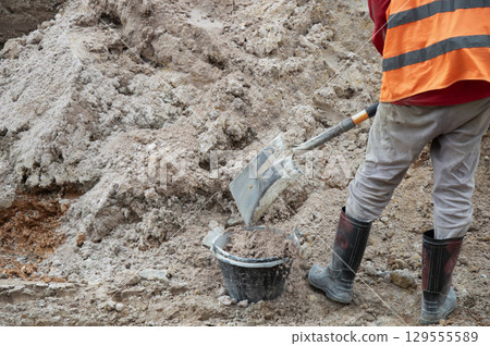 Workers are scooping sand into buckets at a construction site. Workers are scooping sand into buckets at a construction site. 129555589