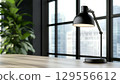 A sleek black desk lamp illuminating a modern workspace with large windows and city view 129556612