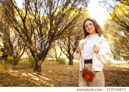 Smiling young woman with the photo camera walking in the park Smiling young woman with the photo camera walking in the park 129556671