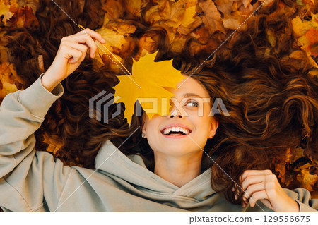 Smiling young woman lies on the autumn foliage in the forest with the yellow leaves 129556675
