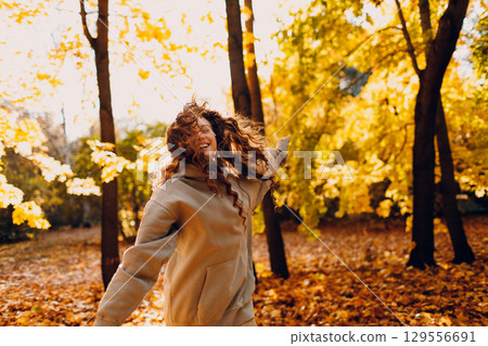 Smiling young woman enjoys the autumn weather in the forest with the yellow leaves at sunset 129556691