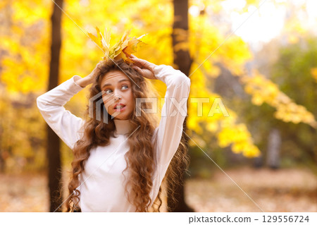 Smiling young woman enjoys the autumn weather in the forest with the yellow leaves at sunset 129556724
