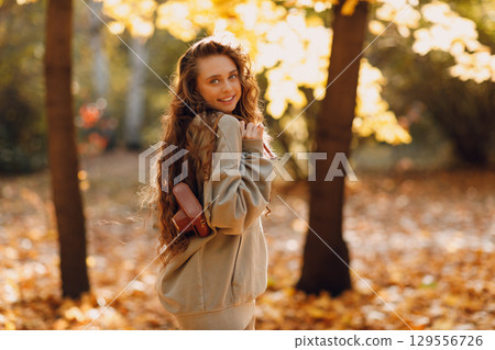Smiling young woman walking in autumn forest with the yellow leaves at sunset Smiling young woman walking in autumn forest with the yellow leaves at sunset 129556726
