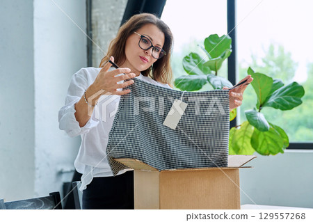 Happy satisfied woman unpacking online purchase, looking at new clothes 129557268