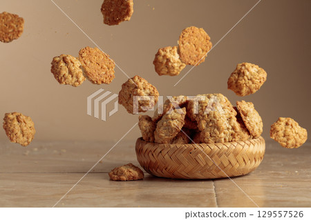 Oatmeal cookies in motion on a beige background. Oatmeal cookies in motion on a beige background. 129557526