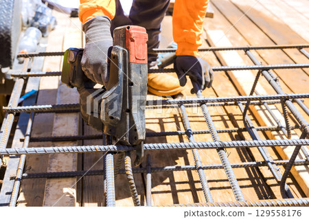 Construction worker using assembling gun on steel reinforcement bars at abuilding site during works day hours 129558176