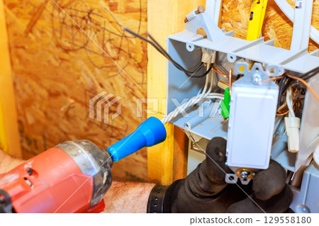Electrician installing switch inside wooden wall with use of drill during renovation work 129558180