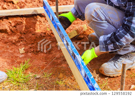 Worker leveling wooden form for concrete slab in outdoor construction site during works day Worker leveling wooden form for concrete slab in outdoor construction site during works day 129558192