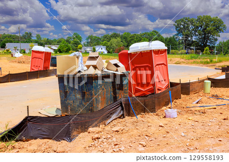 Construction site with portable toilets, debris under bright blue sky during works day 129558193