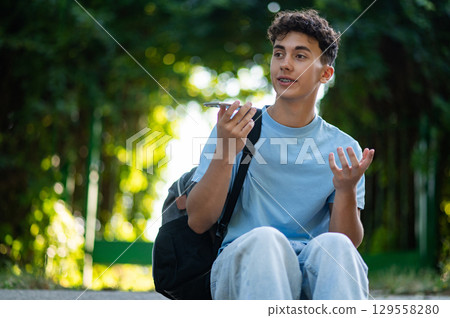 Handsome teen in the park recording a voice message Handsome teen in the park recording a voice message 129558280