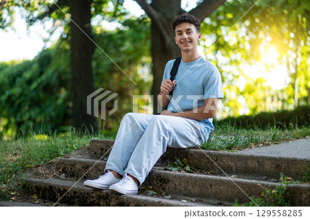Handsome teen in the park sitting on the steps and smiling 129558285