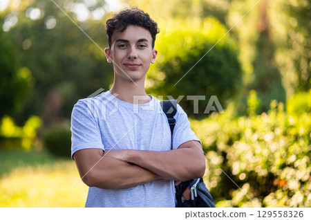 Dark-haired teen looking confident and smiling while standing in the park 129558326