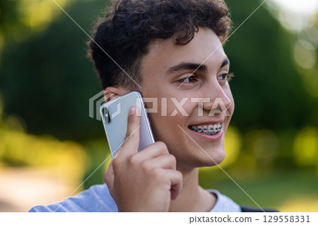 Dark-haired teen with a phone in hands in the park Dark-haired teen with a phone in hands in the park 129558331
