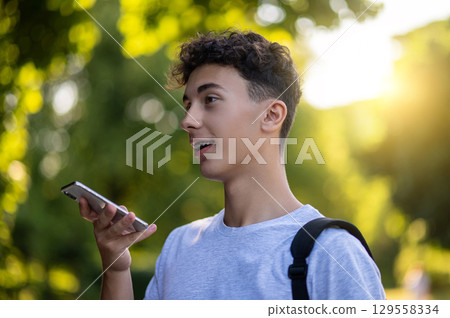 Dark-haired teen with a phone in hands in the park 129558334