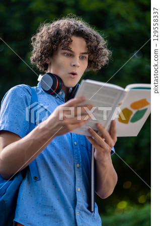 Teen reading a book and looking surprised and impressed Teen reading a book and looking surprised and impressed 129558337