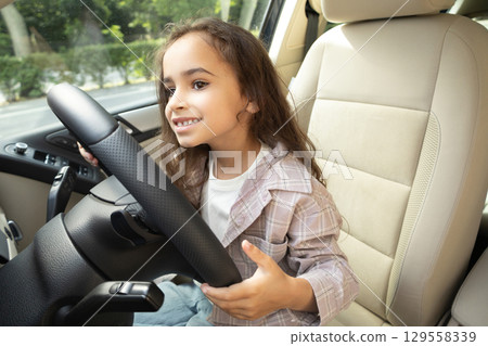 Cute little girl sitting at the steering wheel in a car and feeling excited 129558339