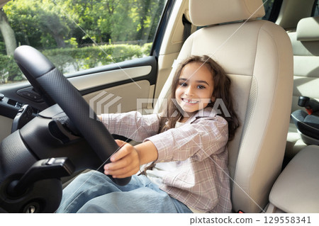 Cute little girl sitting at the steering wheel in a car and feeling excited 129558341