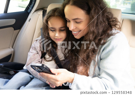 Mom and daughter spending time together and watching something while sitting in a car 129558348