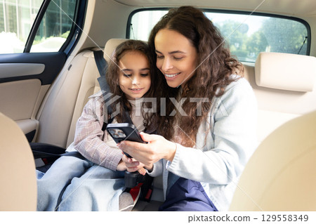 Mom and daughter spending time together and watching something while sitting in a car 129558349
