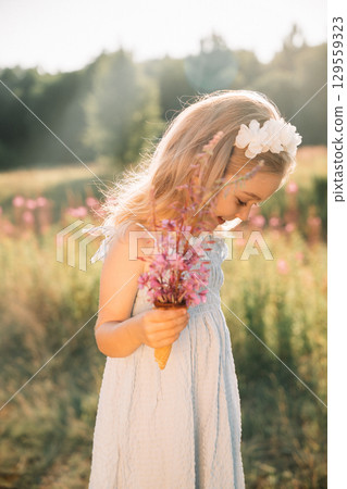 Young girl enjoys a sunny day in a field holding flowers and an ice cream cone 129559323