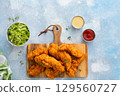 Chicken tenders served on a wooden board with salad and sauces 129560727