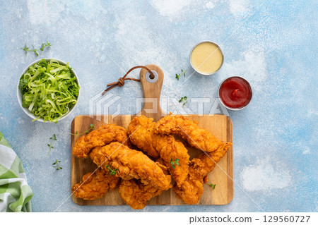 Chicken tenders served on a wooden board with salad and sauces Chicken tenders served on a wooden board with salad and sauces 129560727