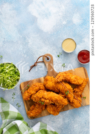 Chicken tenders served on a wooden board with salad and sauces Chicken tenders served on a wooden board with salad and sauces 129560728