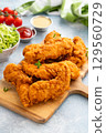 Chicken tenders served on a wooden board with salad and sauces 129560729
