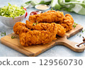 Chicken tenders served on a wooden board with salad and sauces 129560730