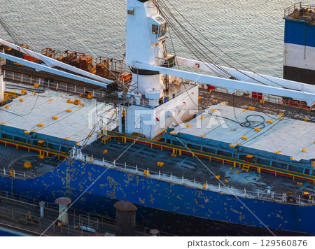 A detailed view of a blue cargo ship with visible wear and rust, docked at a shipyard in Riga, Latvia, with cranes and dock infrastructure in the background. A detailed view of a blue cargo ship with visible wear and rust, docked at a shipyard in Riga, Latvia, with cranes and dock infrastructure in the background. 129560876