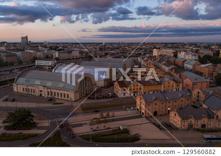 Riga Central Market pavilions and colorful historic buildings under a pink and blue sunset sky with scattered clouds in Riga, Latvia. Riga Central Market pavilions and colorful historic buildings under a pink and blue sunset sky with scattered clouds in Riga, Latvia. 129560882