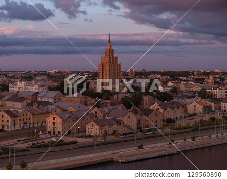 The Latvian Academy of Sciences stands at the center, surrounded by historic buildings. A waterfront area and soft pink and purple skies complete the scene. 129560890