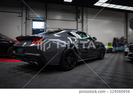 A sleek gray Ford Mustang GT 5.0 with black alloy wheels and dual exhaust is showcased indoors on a checkered floor in a professional garage setting. 129560956