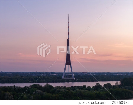 The Riga TV Tower stands tall against a pink and orange sunset sky, with a calm river and greenery below, showcasing its unique tripod design. The Riga TV Tower stands tall against a pink and orange sunset sky, with a calm river and greenery below, showcasing its unique tripod design. 129560983