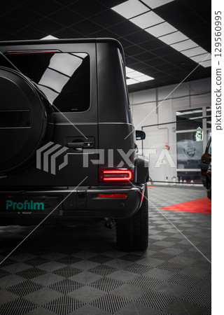 Matte black Mercedes AMG G Class SUV parked indoors on a checkered floor with red carpet, showcasing spare tire cover and LED taillights. Matte black Mercedes AMG G Class SUV parked indoors on a checkered floor with red carpet, showcasing spare tire cover and LED taillights. 129560995