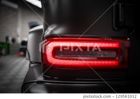 Close up view of the Mercedes AMG G Class rear taillight with rectangular LED design, matte black exterior, and blurred indoor showroom background. Close up view of the Mercedes AMG G Class rear taillight with rectangular LED design, matte black exterior, and blurred indoor showroom background. 129561012