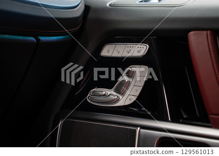 Interior door panel of a Mercedes AMG G Class featuring metallic seat adjustment controls, black leather with red stitching, and a red leather armrest. 129561013